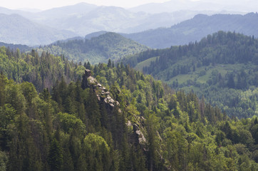 Fototapeta na wymiar Dovbush Rocks - the famous landmark of the Carpathians, view from the neighboring mountain; Two flags on the top