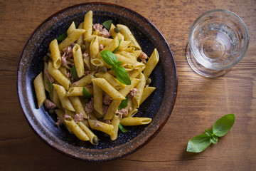 Tuna, basil and caper penne with pesto sauce in bowl on wooden background. Pasta with tuna fish. overhead, horizontal