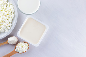 Assorted dairy products on a white board, cottage cheese, cream and soft cheese on a white background, milk in a glass, soft cheese for sandwiches, wooden cutlery, copy space