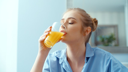 Portrait of happy young woman drinking orange juice during breakfast.