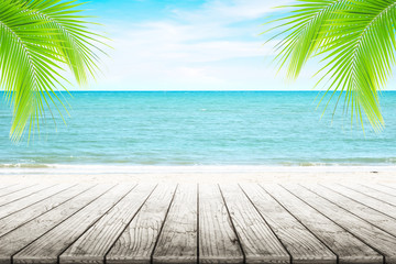 Empty wooden table and palm leaves with party on beach blurred background in summer time.