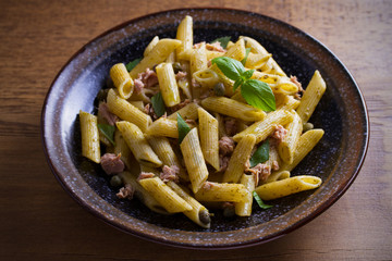 Tuna, basil and caper penne with pesto sauce in bowl on wooden background. Pasta with tuna fish. overhead, horizontal