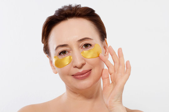 Middle aged woman with collagen pads under her eyes isolated on white background. Eye patch on face. Spa concept. Copy space