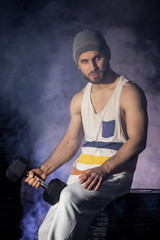 athletic handsome muscular man doing exercises with dumbbells in smoke