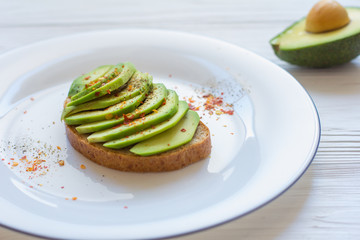 Toast with cutted avocado and spices in white plate on white wooden background. Close-up