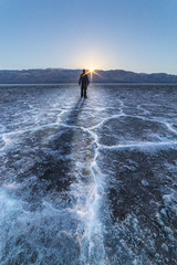 A man stands out in some vast salt flats in the desert, watching the full moon set