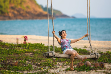 A young mixed race woman swinging on a wooden swing at a seaside tropical beach.