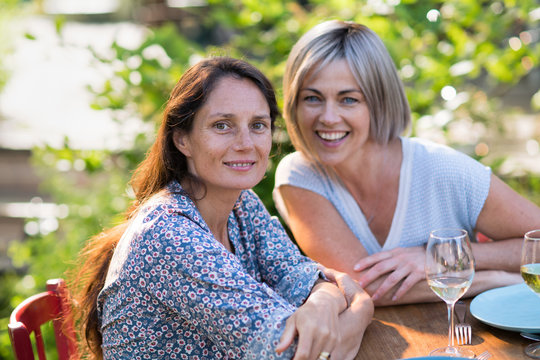  Portrait of two beautiful women in their forties. They are posing for the photo sits on a terrace in front of a glass of wine.