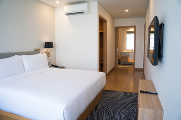 Small hotel room interior with double bed and bathroom. Double bed with white sheets complemented with wall lamp, TV and air conditioner. Hotel room concept - obrazy, fototapety, plakaty