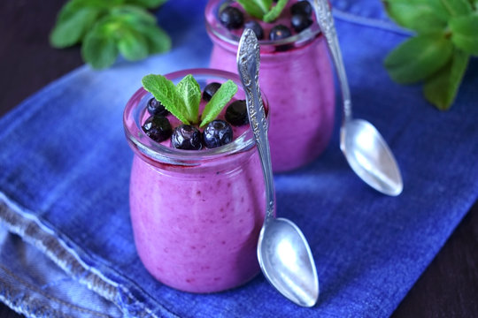 Blueberry smoothie in glass jars topped with berries and mint on blue background