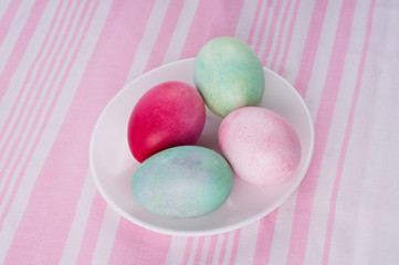 four multicolored painted Easter eggs on a white plate and  striped pink-white tablecloth. holiday easter greeting card, poster, wallpaper