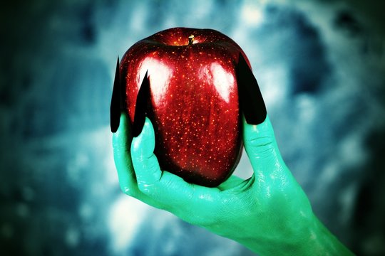 Beautiful red apple in green hands of old witch with black nails.Fairytale scary. mystical and fantasy scene with green hands and red apple.
