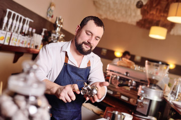 a handsome, bearded barista man holding a Holder with ground coffee. Making coffee in a coffee house