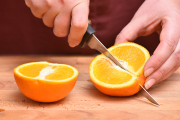 Female hands cut knife orange, juicy and ripe
