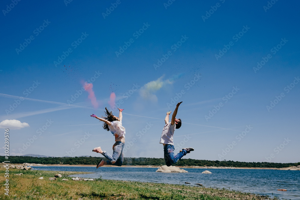 Wall mural Lovely couple having fun outdoors playing with colorful holi powder jumping and laughing. Lifestyle portrait