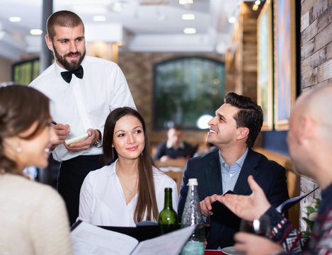 Waiter with notebook taking order from friendly company indoors