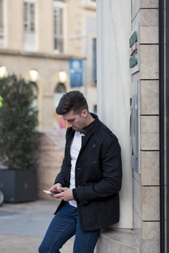 handsome young man with black jacket standing on the street using mobile phone