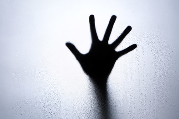 Hand silhouette behind a glass with water drops