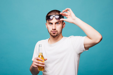 Portrait of a happy summer young in sunglasses man holding beer bottles isolated over green background