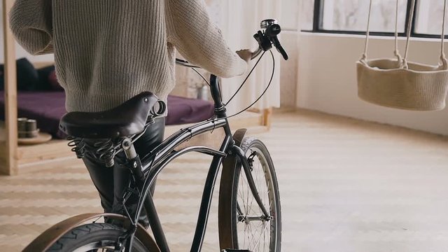 Cropped closeup, rear view of a girl resting on the handlebar of her vintage fixed gear bike on indoors
