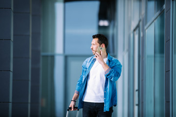 young businessman walking through the financial district of the city with his smartphone and suitcase. business concept