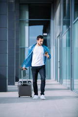 young businessman walking through the financial district of the city with his smartphone and suitcase. business concept