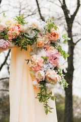Wedding arch decorated with cloth and flowers outdoors. Beautiful wedding set up. Wedding ceremony on green lawn in the garden. Part of the festive decor, floral arrangement.