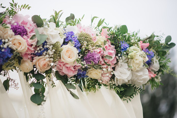 Wedding arch decorated with cloth and flowers outdoors. Beautiful wedding set up. Wedding ceremony on green lawn in the garden. Part of the festive decor, floral arrangement.