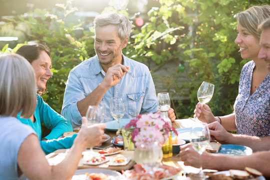 Group of friends gathered around a table in a garden on a summer evening to share a meal and have a good time together - Powered by Adobe
