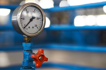 Close-up of a pressure gauge psi meter. Pressure meter and red faucet with steel blue pipe in...