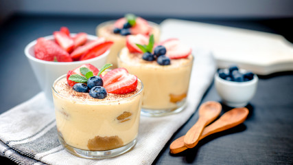homemade, exquisite dessert tiramisu in glasses decorated with strawberry, blueberry, mint on black wooden table