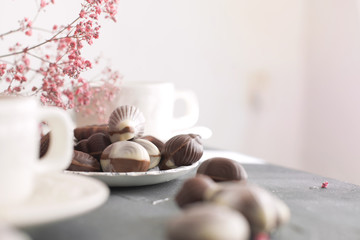 Chocolate sweets in the form of cockleshells and two cups of fragrant coffee. Romantic breakfast. Light colors. Pink flowers
