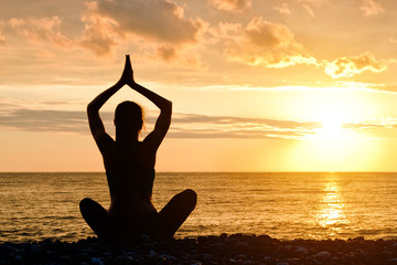 Woman with folded hands over head. Beach, sunset. Silhouette