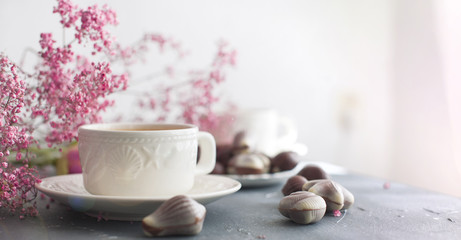A fragrant morning coffee in a white bowl with seashells. Chocolate candies. Pink flowers. Card. Romance