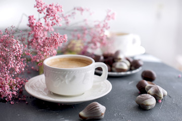 morning coffee in a white cup with seashells. Chocolate candies. Pink flowers. Card
