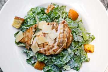 Grilled chicken breast and parmesan cheese salad with dressing, on white plate. Flat lay