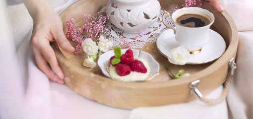 Obraz na płótnie Canvas A woman is drinking coffee in bed. A wooden tray with breakfast. Raspberry berries and flowers. Light colors. Romance. Good morning. Place for text