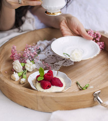 A woman is drinking coffee in bed. A wooden tray with breakfast. Raspberry berries and flowers. Light colors. Romance