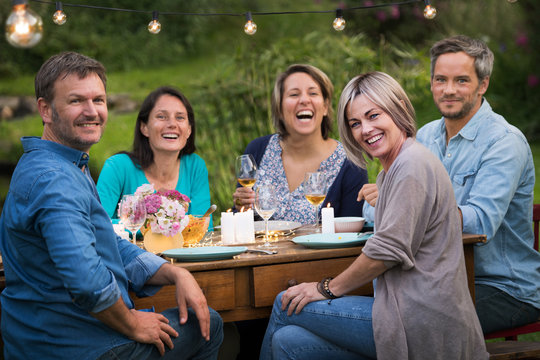 A summer evening of friends in their 40s gather around a table in the garden to share a meal and have fun together.