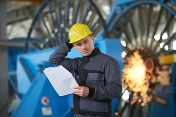 Portrait of young engineer taking notes in factory warehouse room. Industrial manufacturing worker reading documents