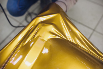 Car wrapping specialist putting vinyl foil or film on car wrapping protective film yacht, boat, ship, car, mobile home. yellow gold film hand pulls