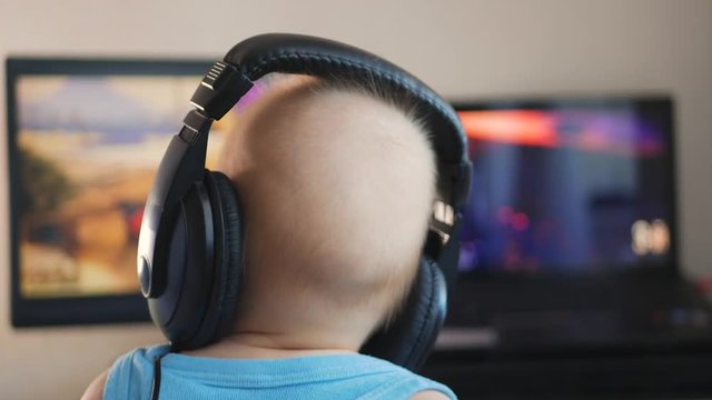 Baby boy in headphones playing the computer game. The concept of computer addiction, selective focus.