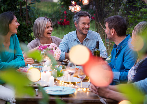 Beautiful summer evening in the garden, a group of friends in their forties have a good time laughing together around a table.