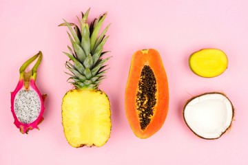 Fototapeta na wymiar Tropical fruit flat lay with pineapple, dragon fruit, papaya, mango, and coconut on a pastel pink background