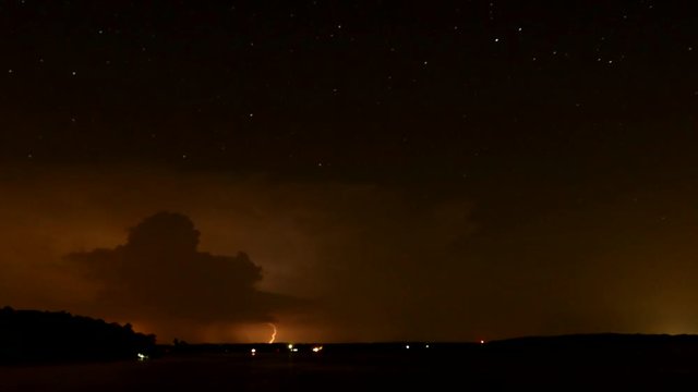 Time lapse of storm at night with lightning reflecting over a lake with stars moving above