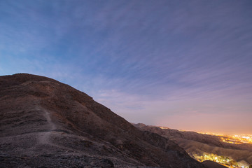 Naklejka na ściany i meble Waypath in the mountains near of Eilat city in the desert in the Israil in the evening with blue sky and city lights
