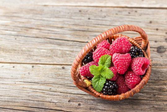 Raspberries and blackberries in a basket on a wooden background.