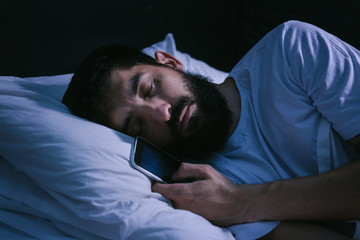 Man sleeping in bed and holding a mobile phone. Concept photo of smart phone addiction.