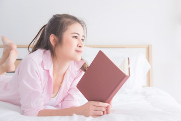 Young asian beautiful woman reading book on bed