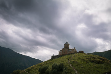 Scenic view on the church on green hill with small country road. Beautiful landscape with mountains on sides.